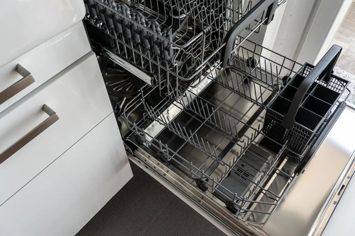 An open dishwasher with empty racks next to white kitchen cabinets
