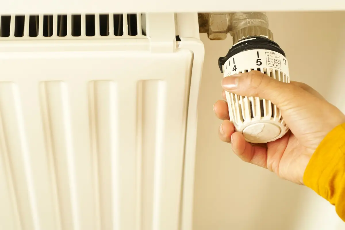 A hand turning the thermostat valve on a white wall radiator