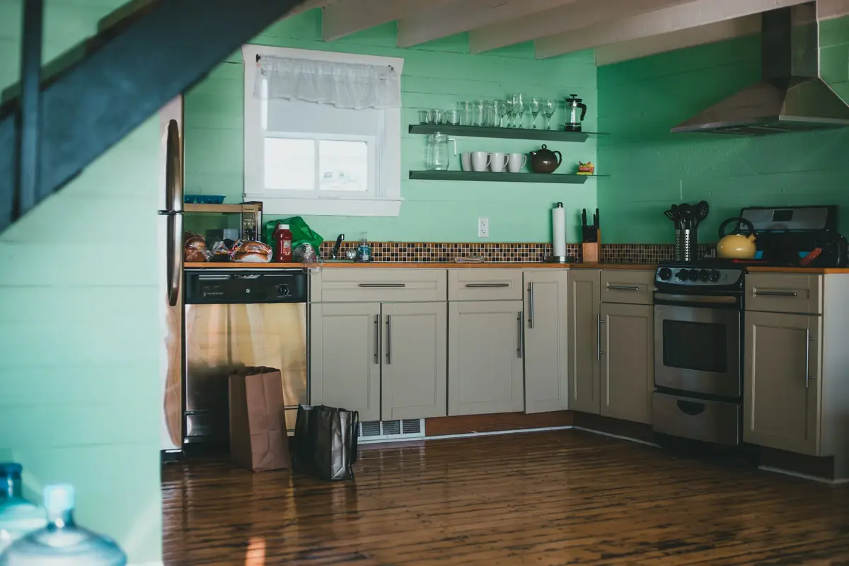 A small home kitchen with mint green walls, wooden floors, open shelves and a gas range