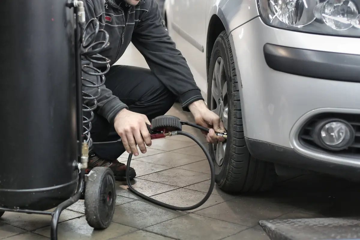 A person filling a car tire with an air hose in a garage