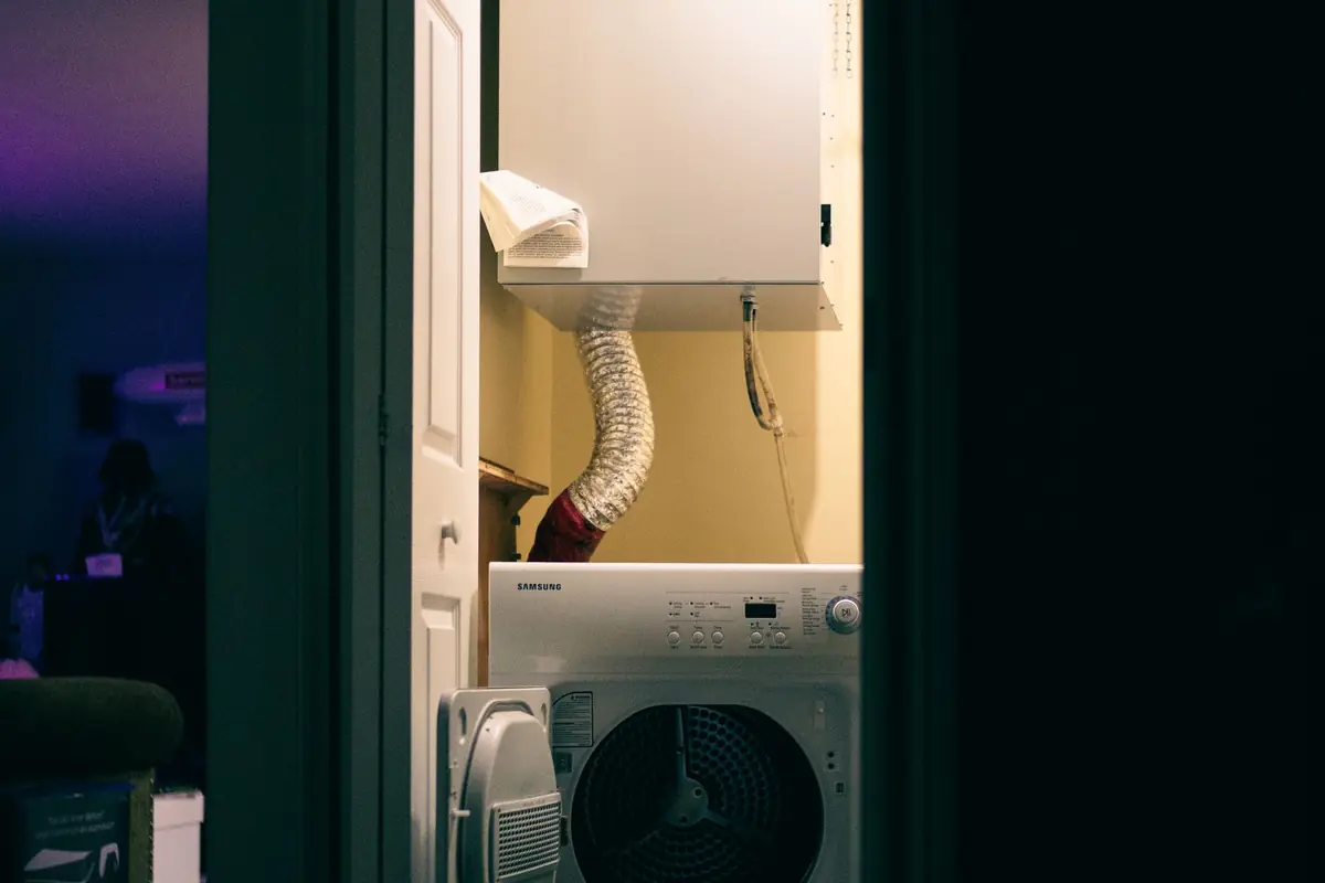 A front-load washer in a narrow laundry closet with a dryer vent hose