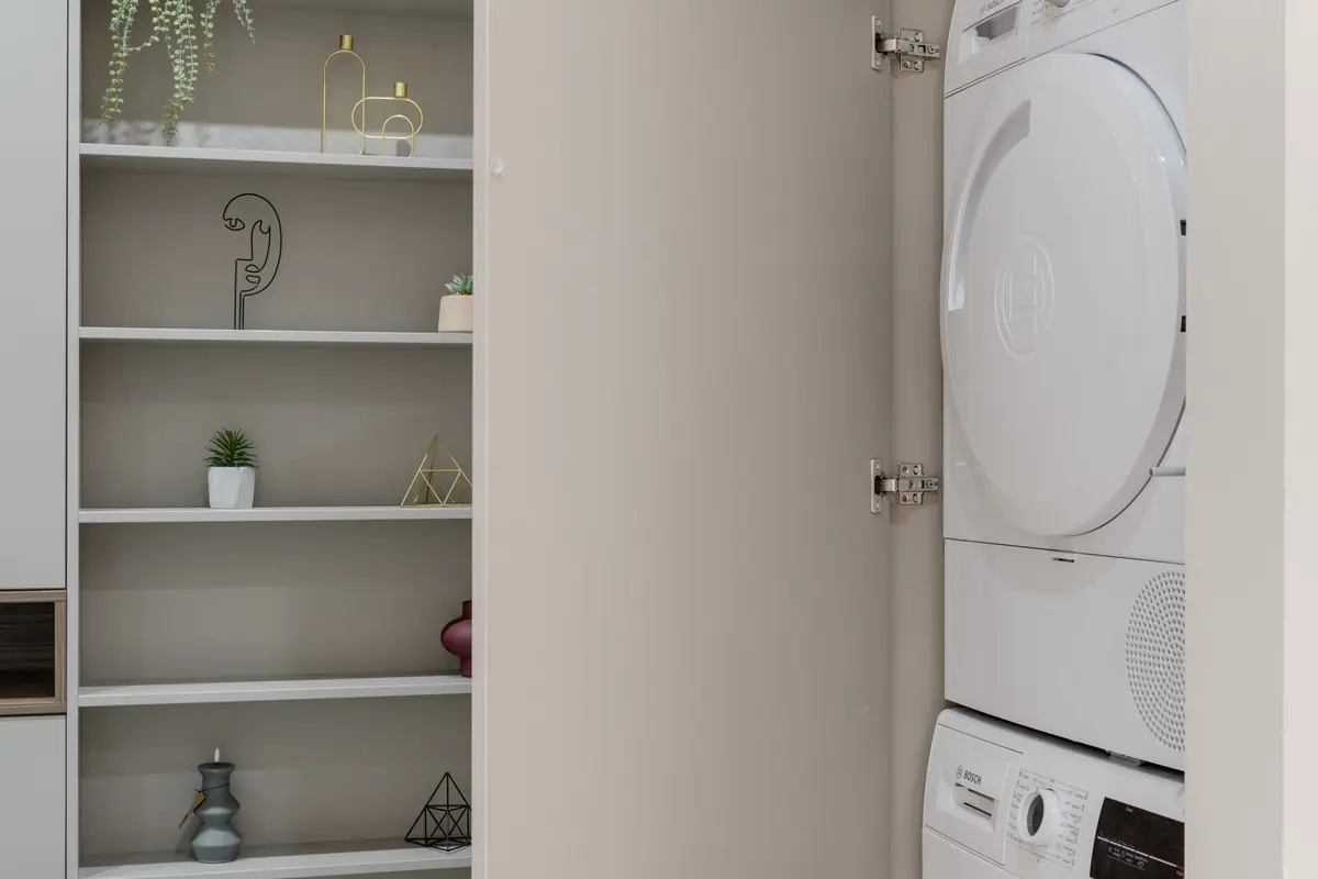 A stacked washer and dryer built into a cabinet beside open shelves