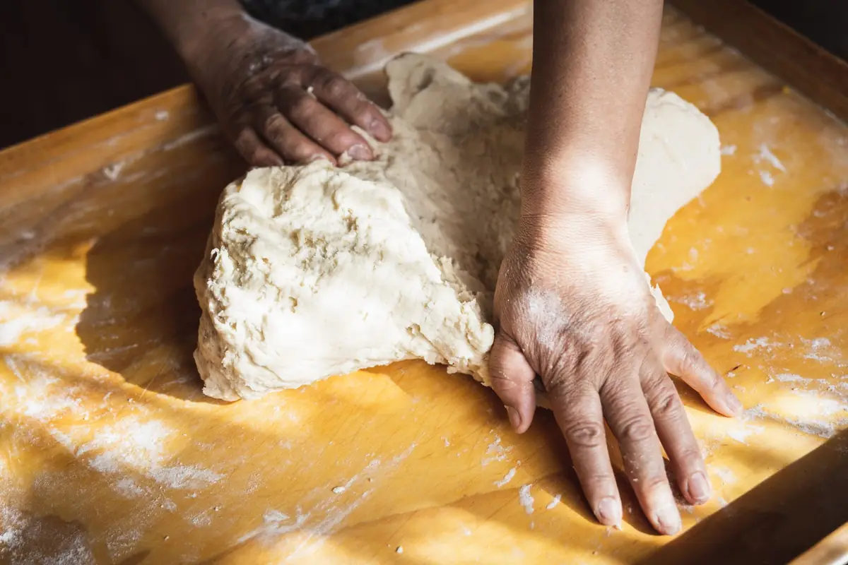 Hands kneading bread dough on a floured counter