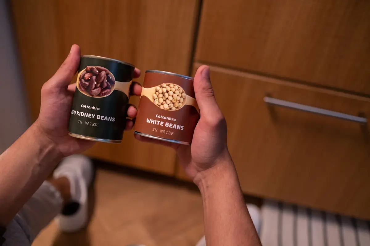 Hands holding two cans of beans in a kitchen