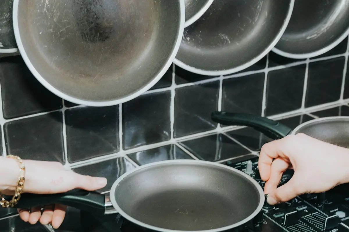 Hands lifting a frying pan off a smooth cooktop under hanging pans