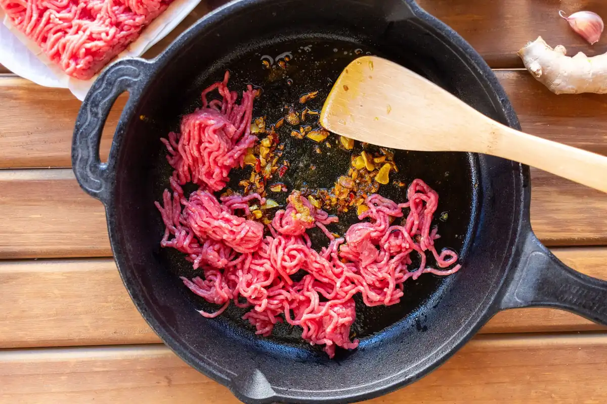 Ground beef browning in a cast iron skillet, showing the pour spout and short helper handle