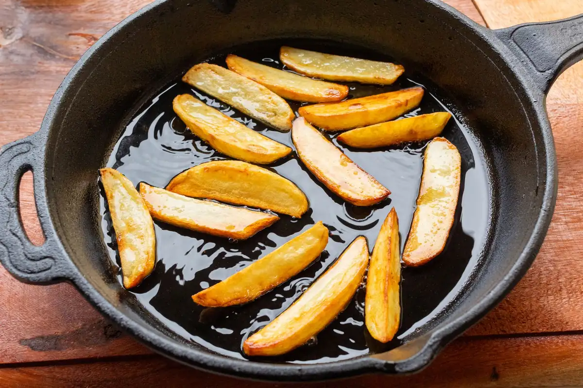 Potato wedges frying in oil in a black cast iron skillet with a helper handle