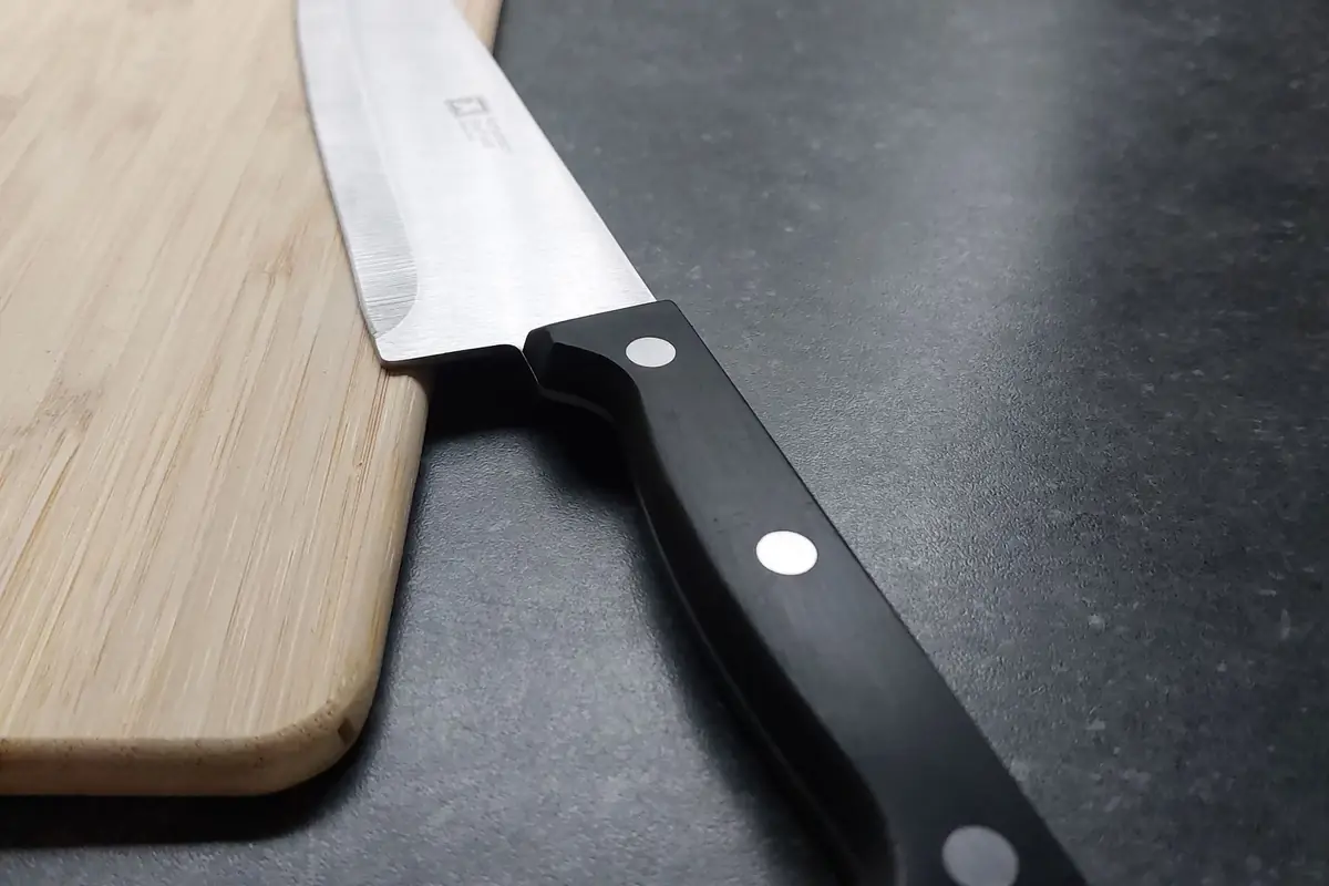 A chef's knife with a black riveted handle resting on a cutting board