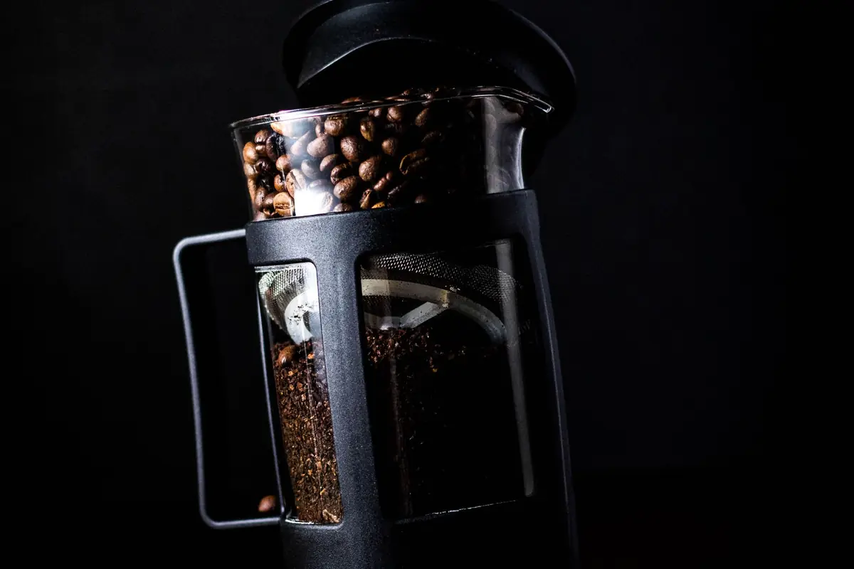 A French press beside whole coffee beans