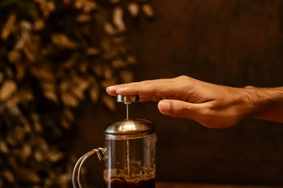 A hand pressing down the plunger of a French press