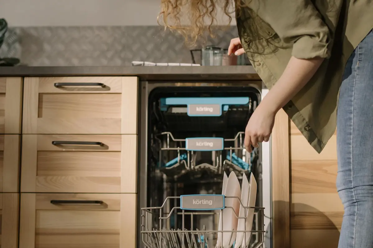 A woman loading dishes into a dishwasher in a small kitchen