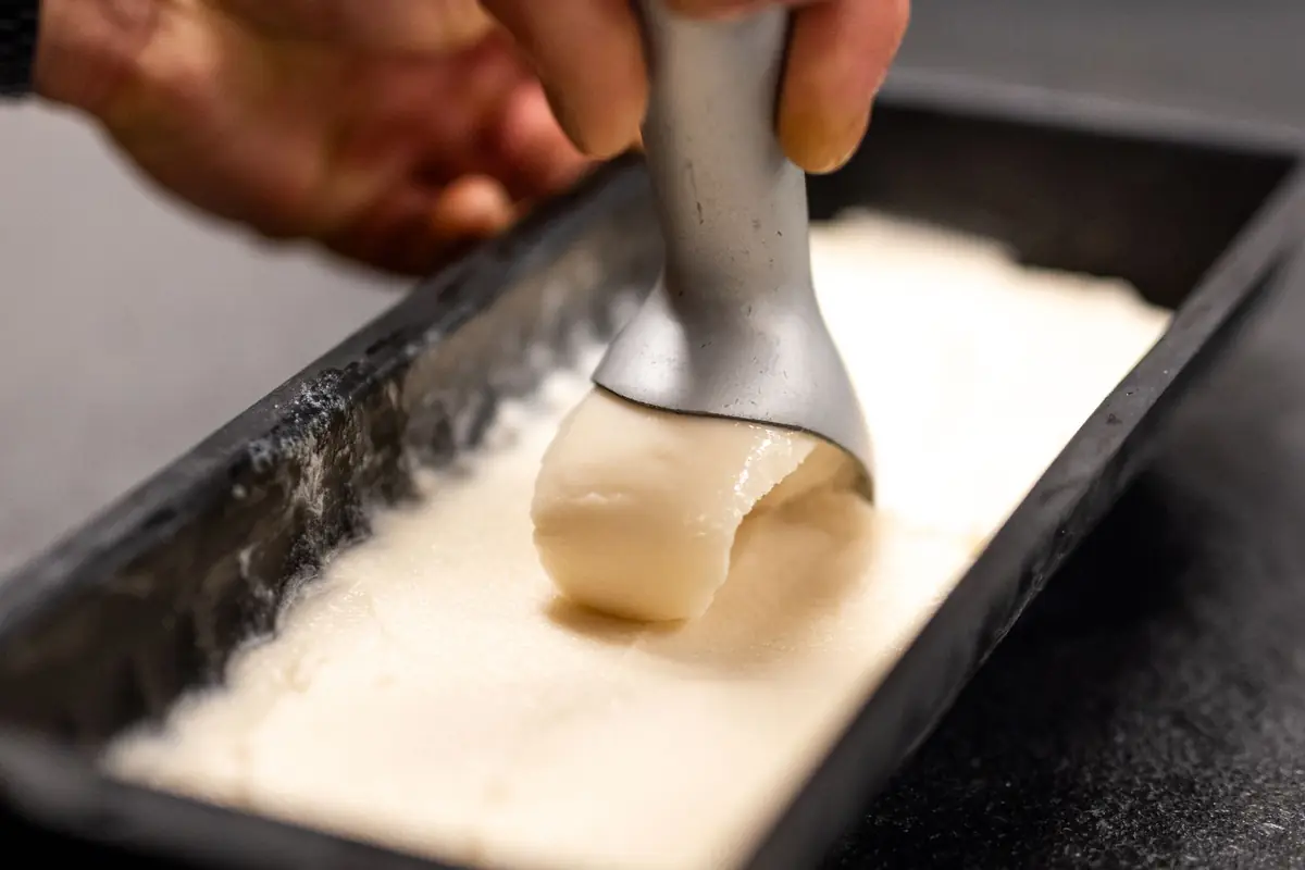 A scoop pulling vanilla ice cream from a metal loaf pan