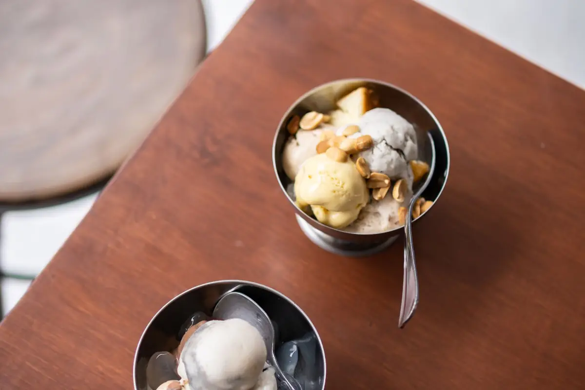 Two metal bowls of ice cream with spoons on a wooden board