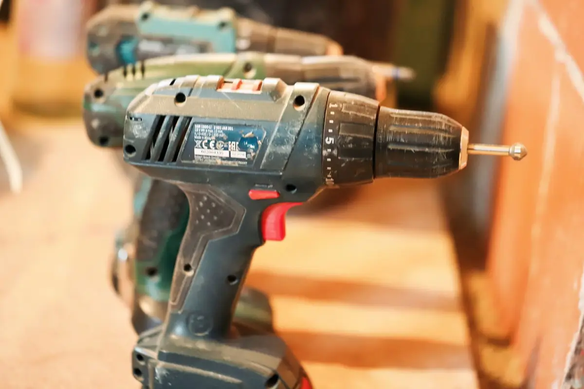A row of cordless drills on a wooden workbench