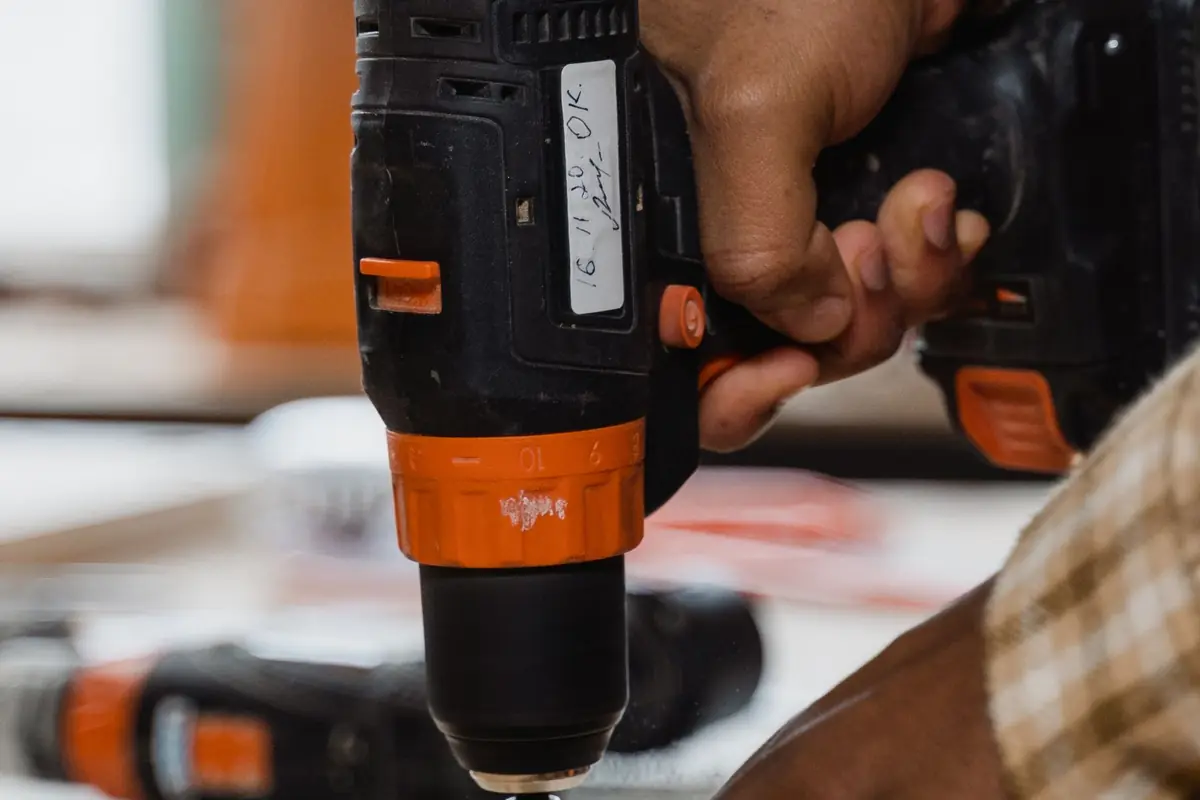 Hands drilling into a wooden board with a cordless drill
