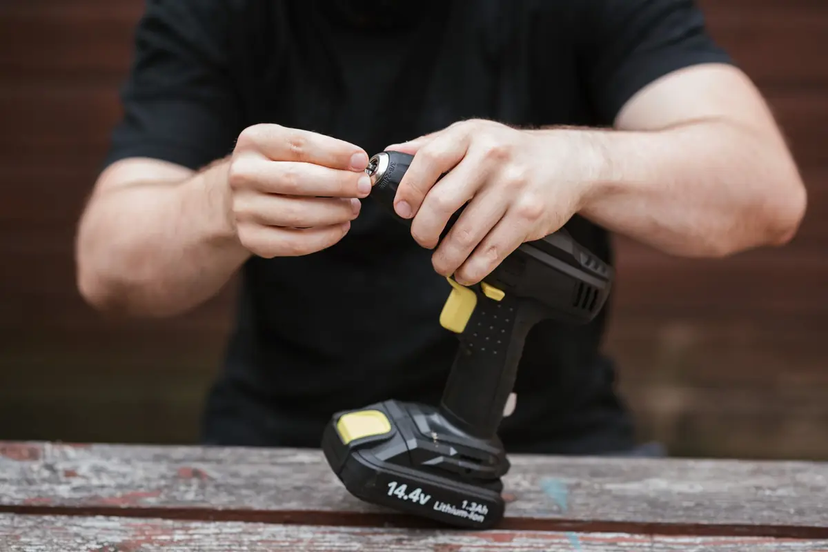 A man tightening a bit in a cordless drill with its battery pack attached