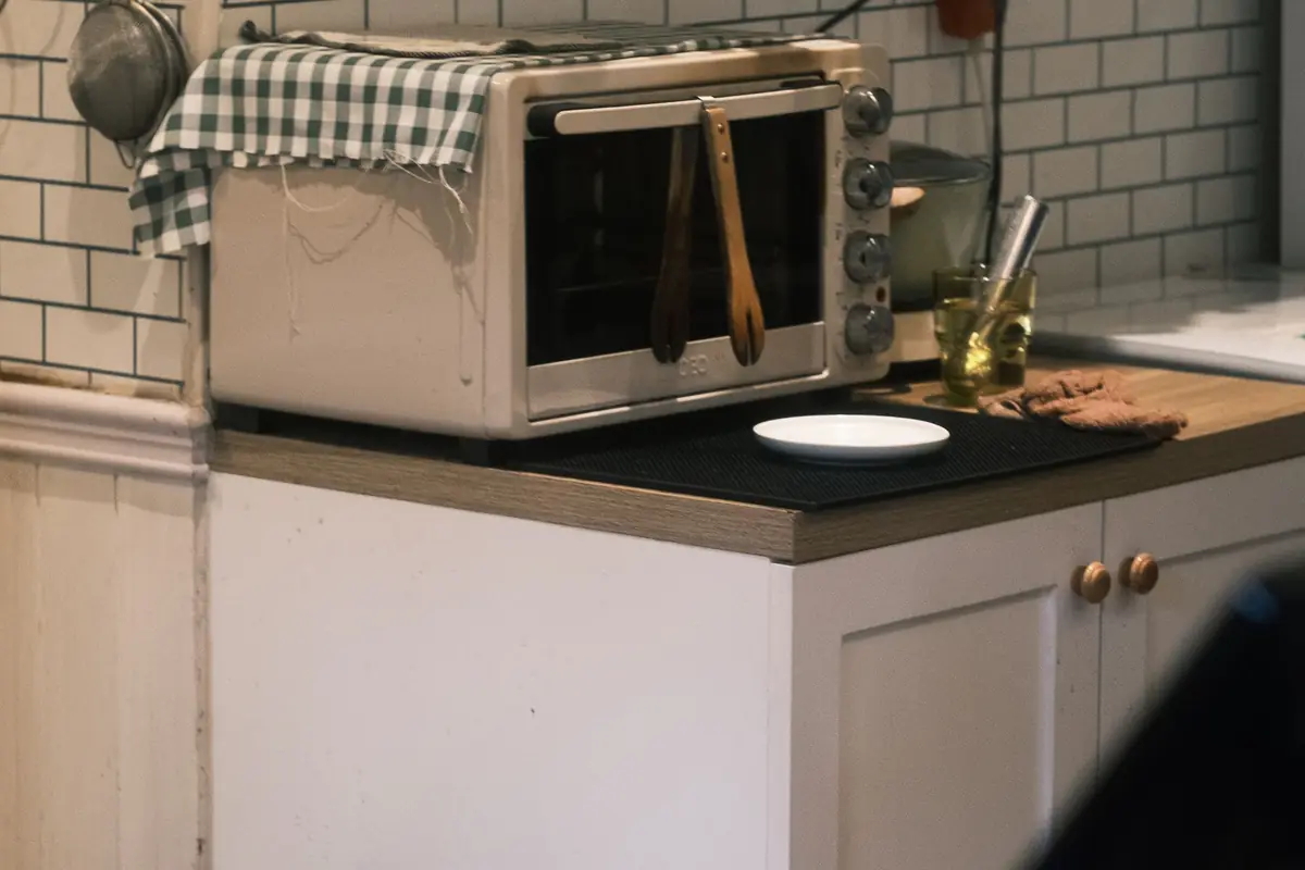 A stainless countertop oven on a kitchen counter against a tiled wall