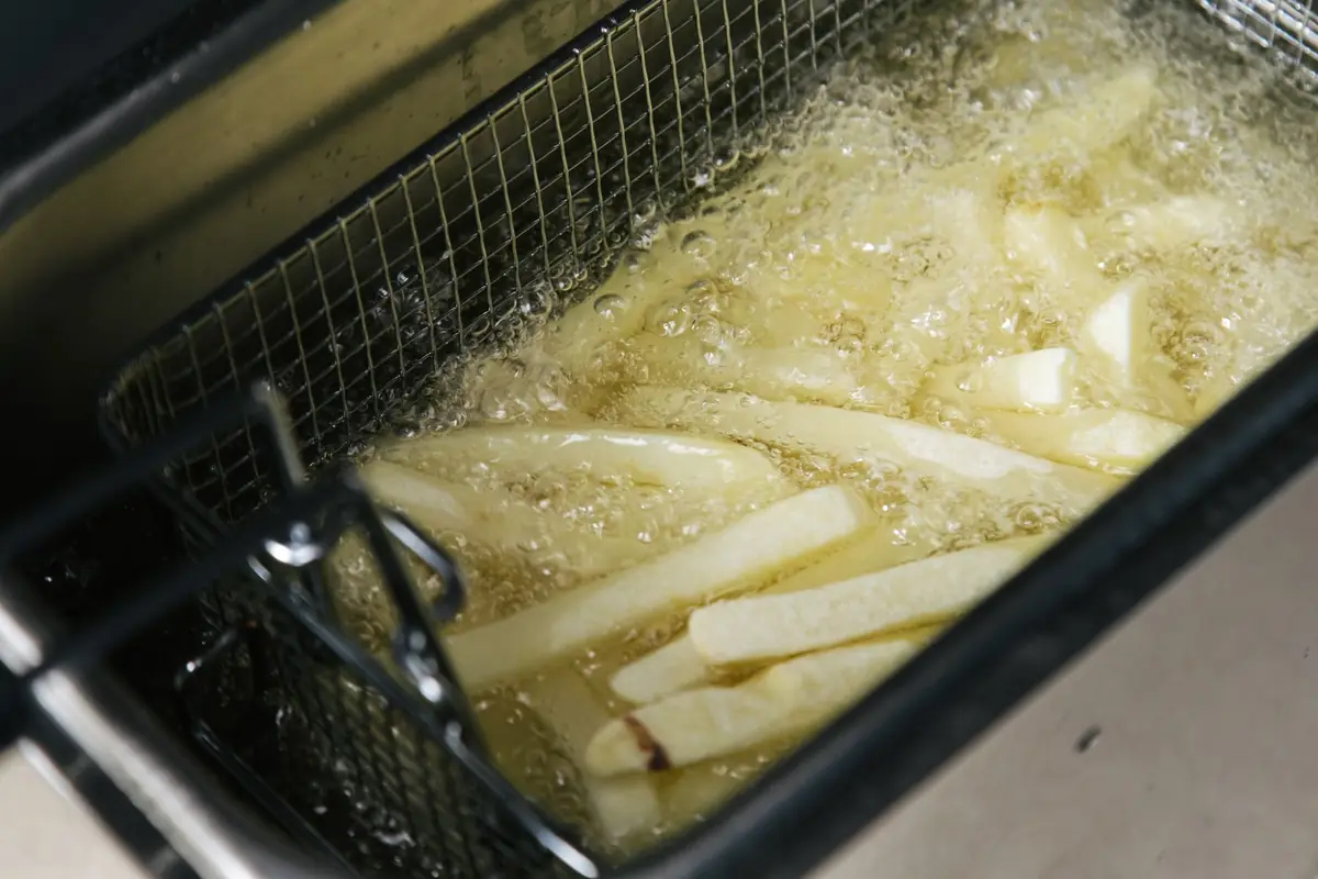 French fries cooking in a deep fryer basket in bubbling oil