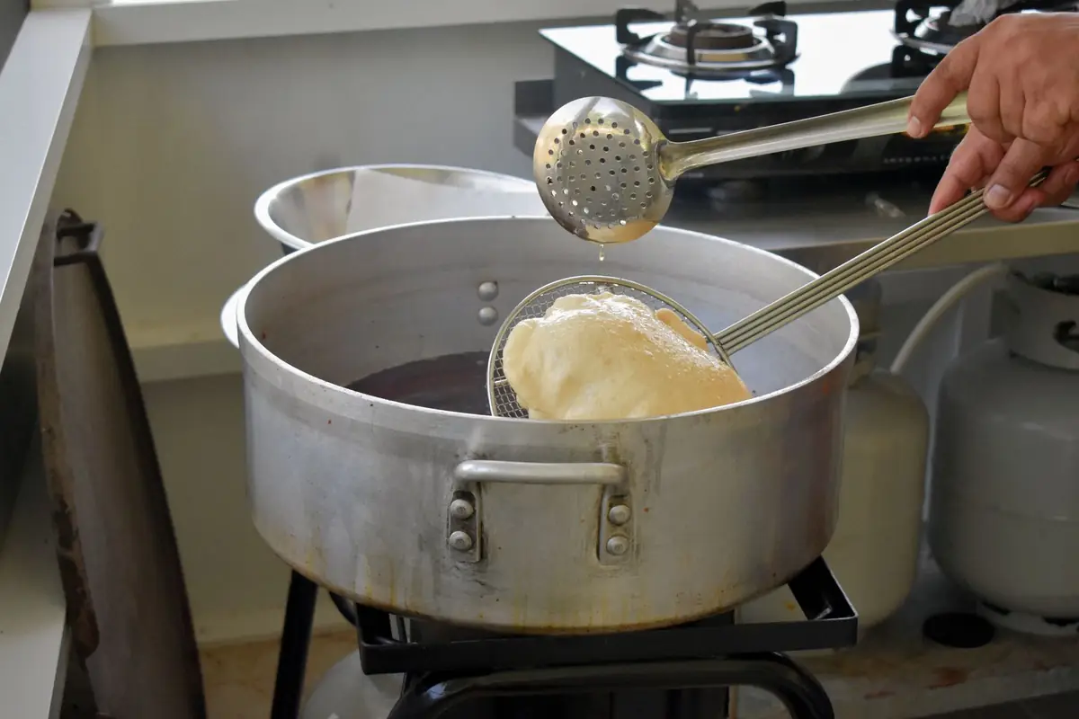 A cook lifting food from a pot of hot oil with a slotted ladle