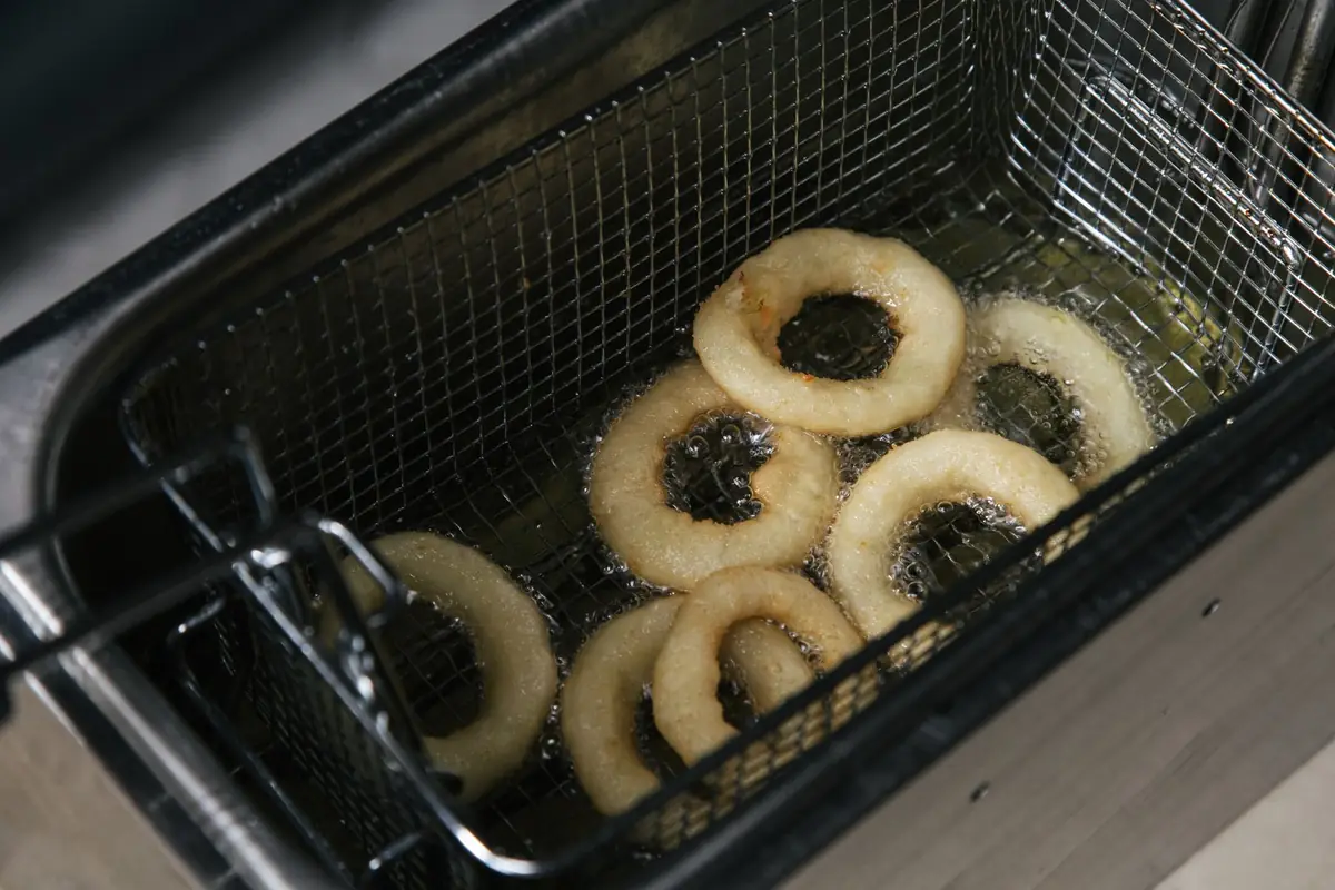 Onion rings frying in a deep fryer basket
