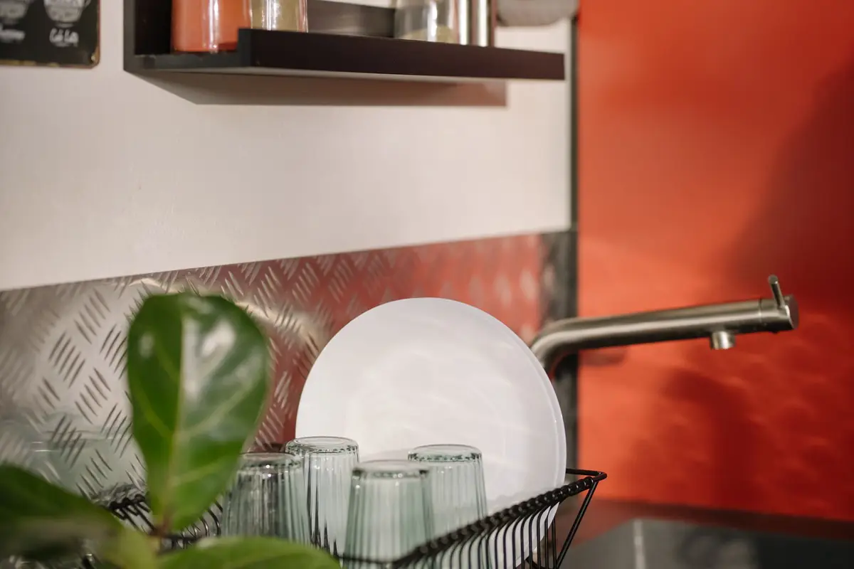 Plates and glasses drying in a wire rack beside a sink with an orange wall