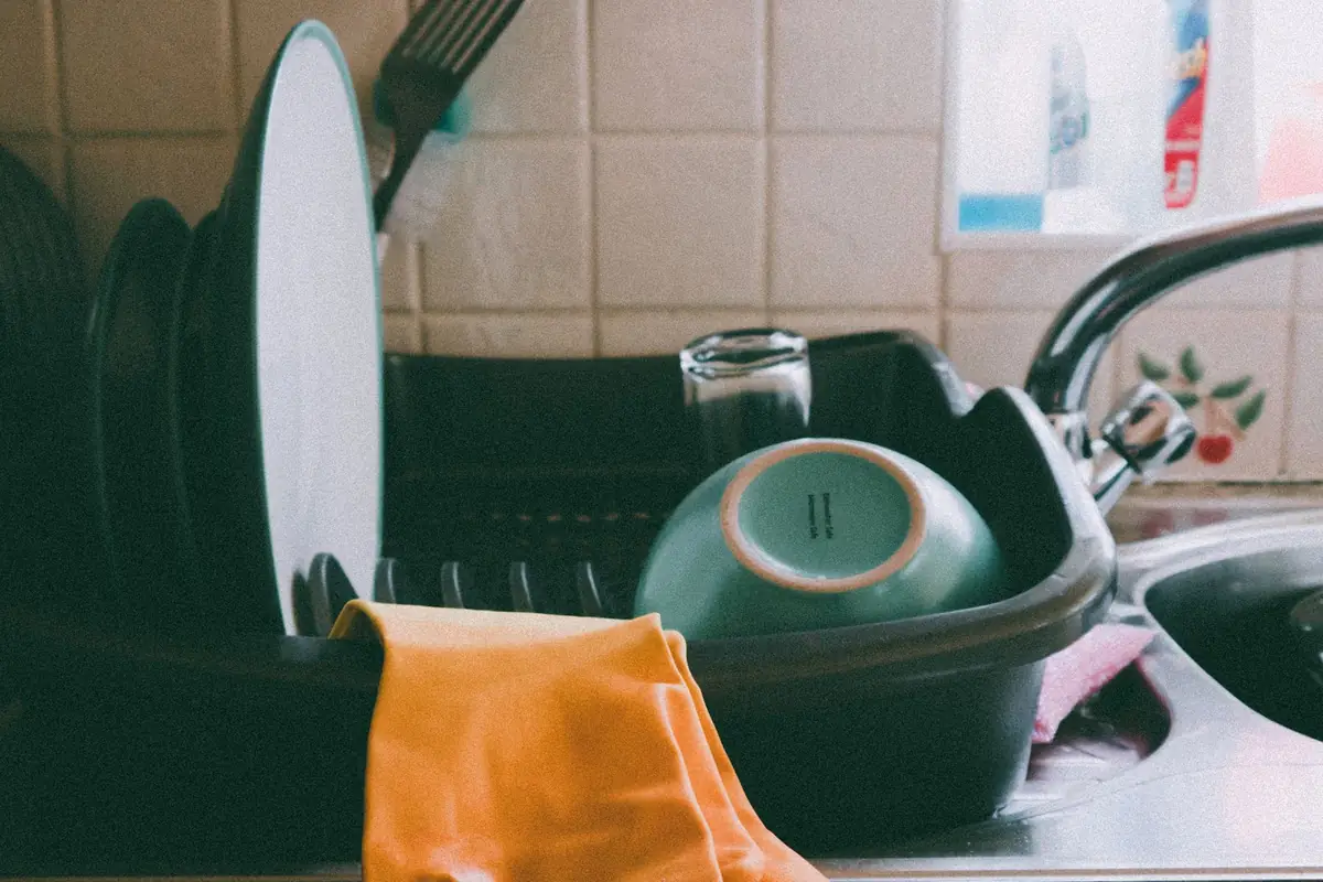 A dish drainer with plates and a bowl next to a sink, with an orange towel over the edge