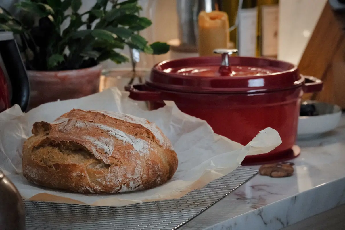 A round sourdough loaf on a counter next to a cast iron Dutch oven