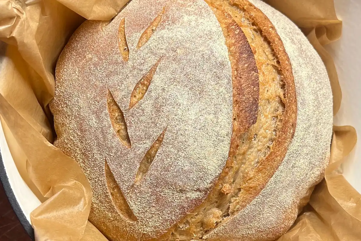 A scored sourdough loaf baked inside a red enameled Dutch oven
