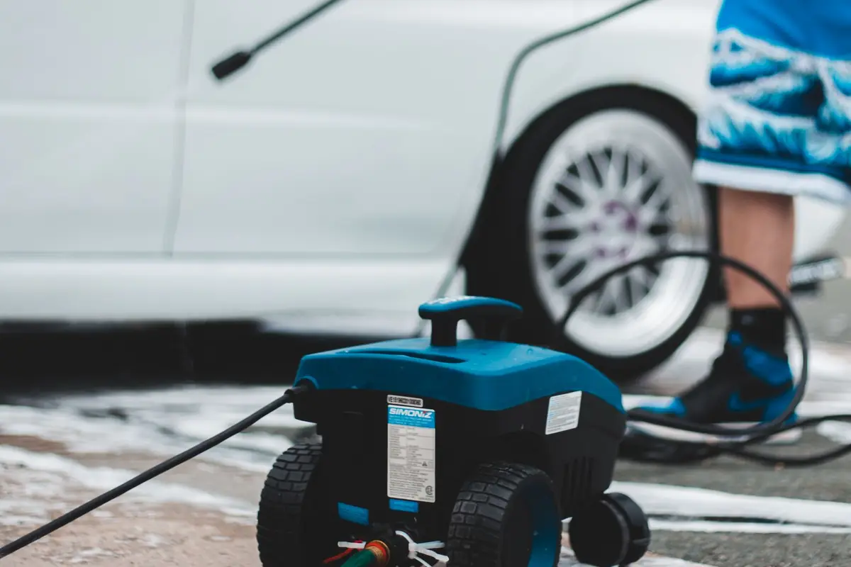 An electric pressure washer on the ground next to a white car