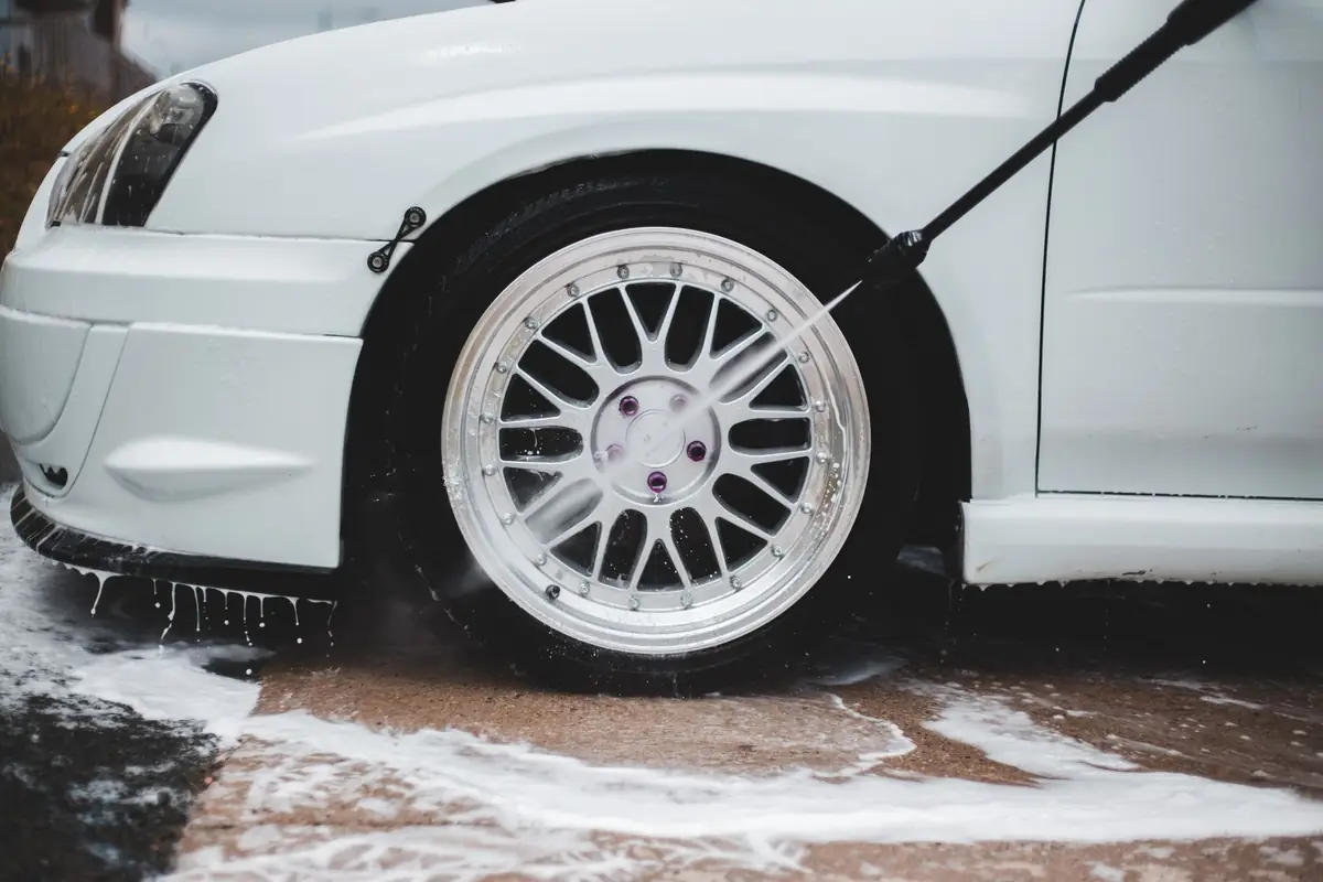 A pressure washer spray rinsing a car wheel