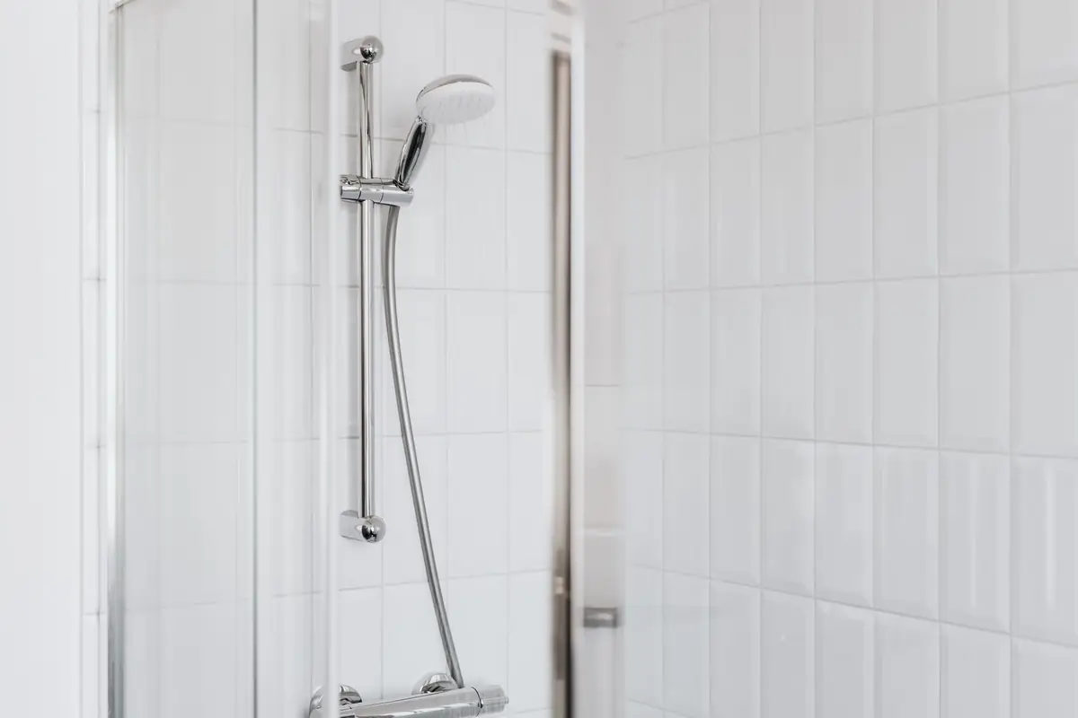 A shower with a chrome slide bar and handheld head in a white-tiled bathroom