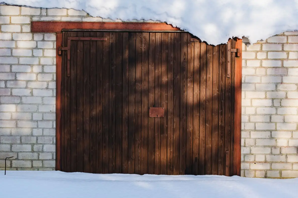 A wooden garage door with snow on the ground in front of it