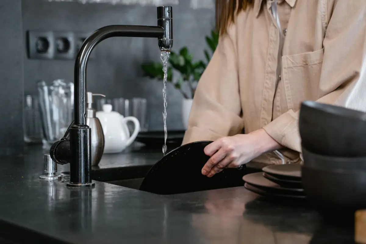 A person rinsing dishes at a black kitchen sink