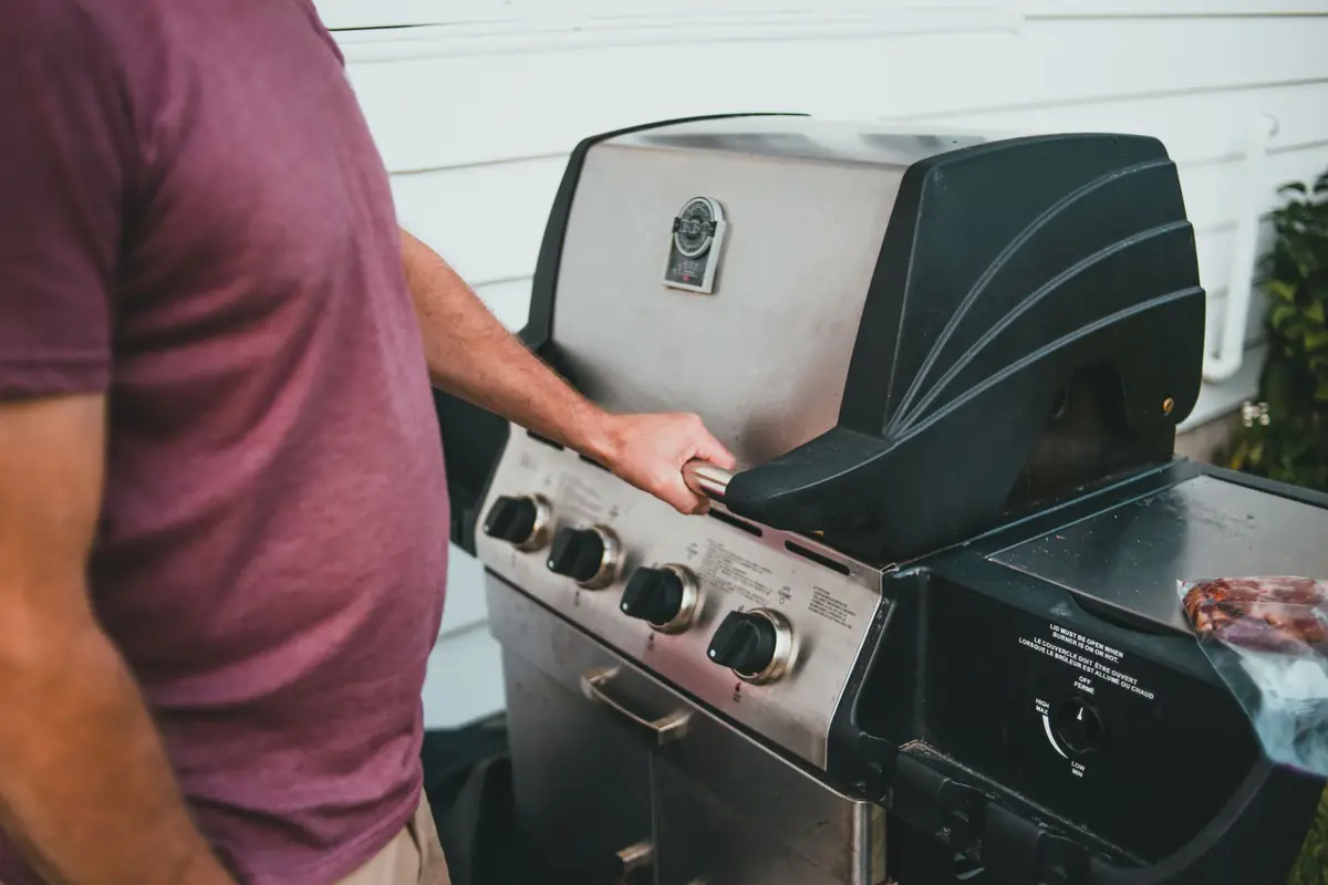 A man turning the knob on a stainless steel gas grill