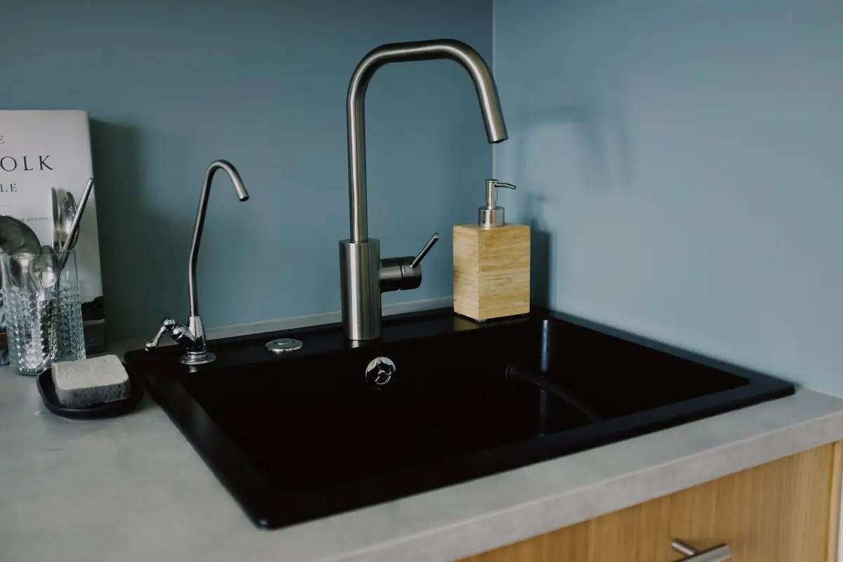 A black kitchen sink with a main faucet and a small separate tap
