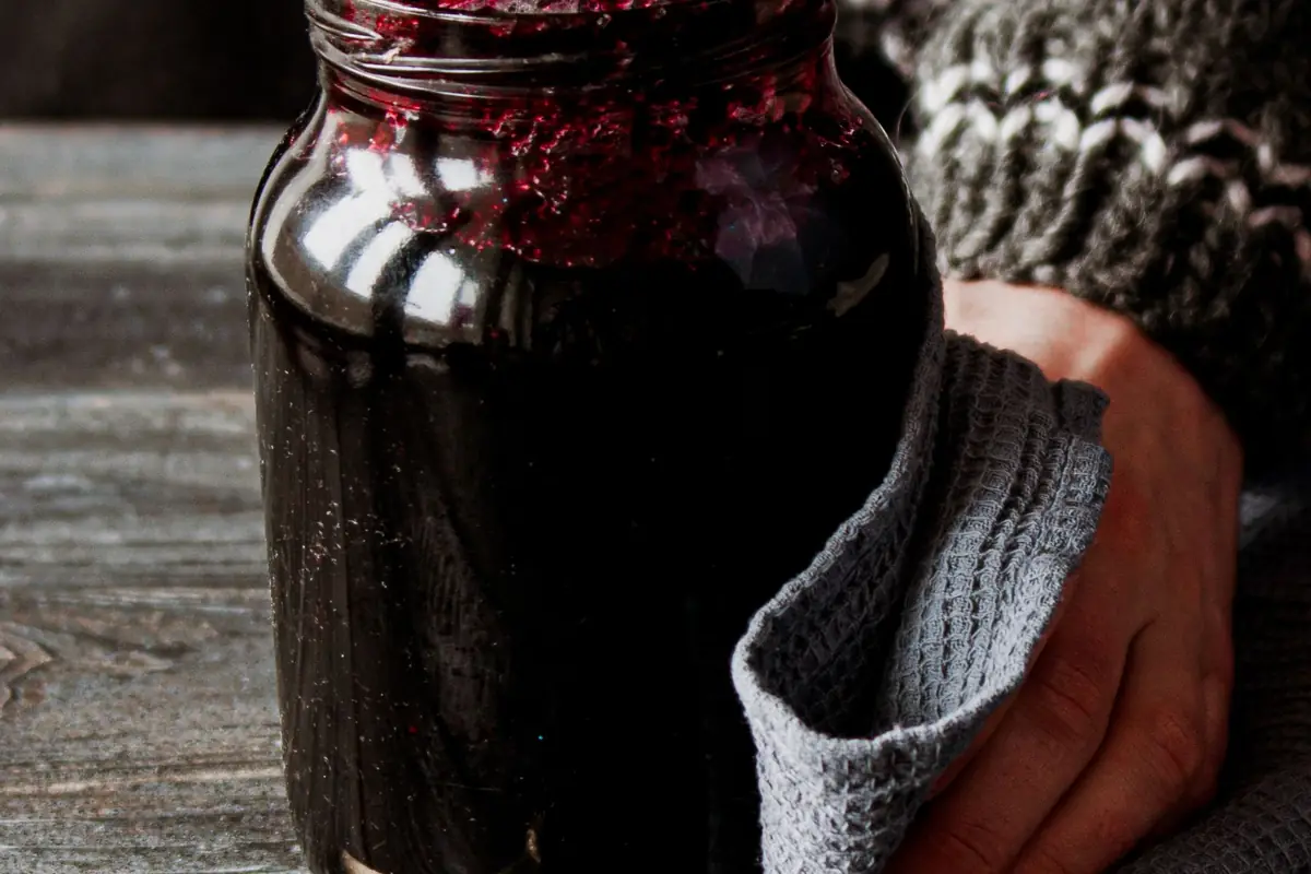 Hands using a dish towel to grip a jar of jam while opening it