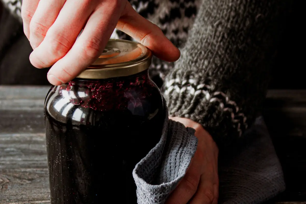 A hand pressing on the lid of a jar of jam