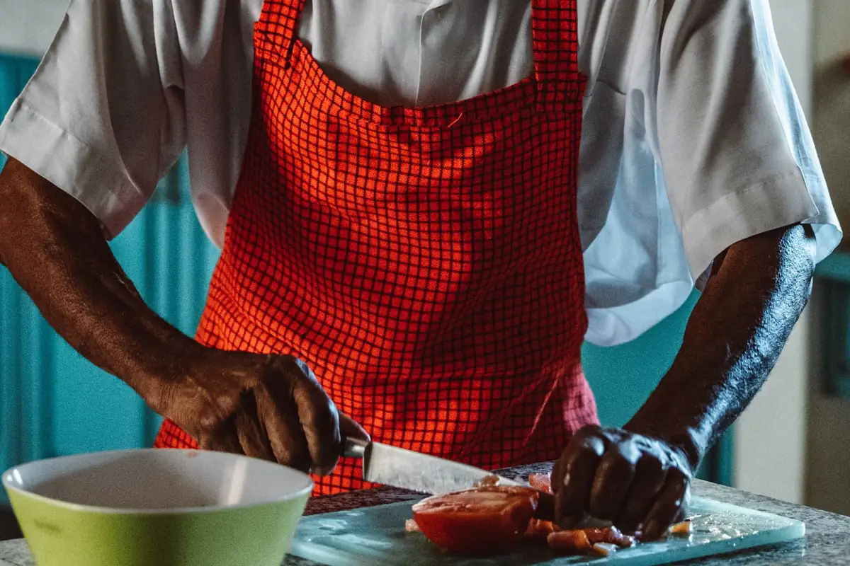 An older man in a red apron slicing tomatoes on a cutting board