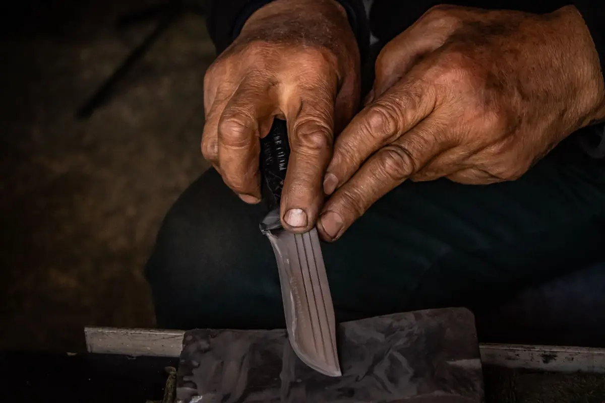 Hands sharpening a kitchen knife on a whetstone