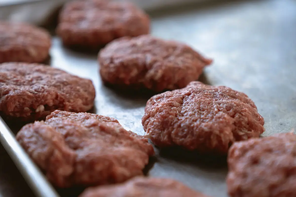 Raw ground meat patties on a metal tray