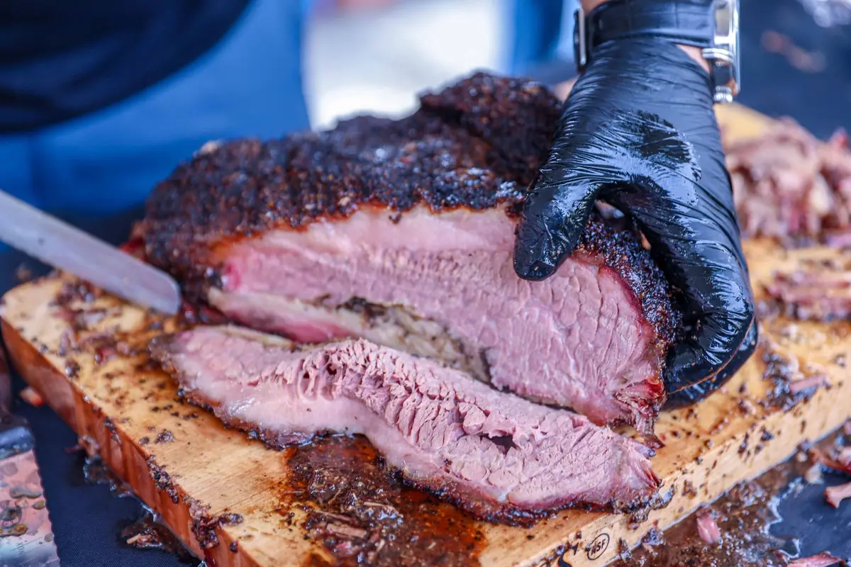 A gloved hand slicing smoked brisket on a cutting board