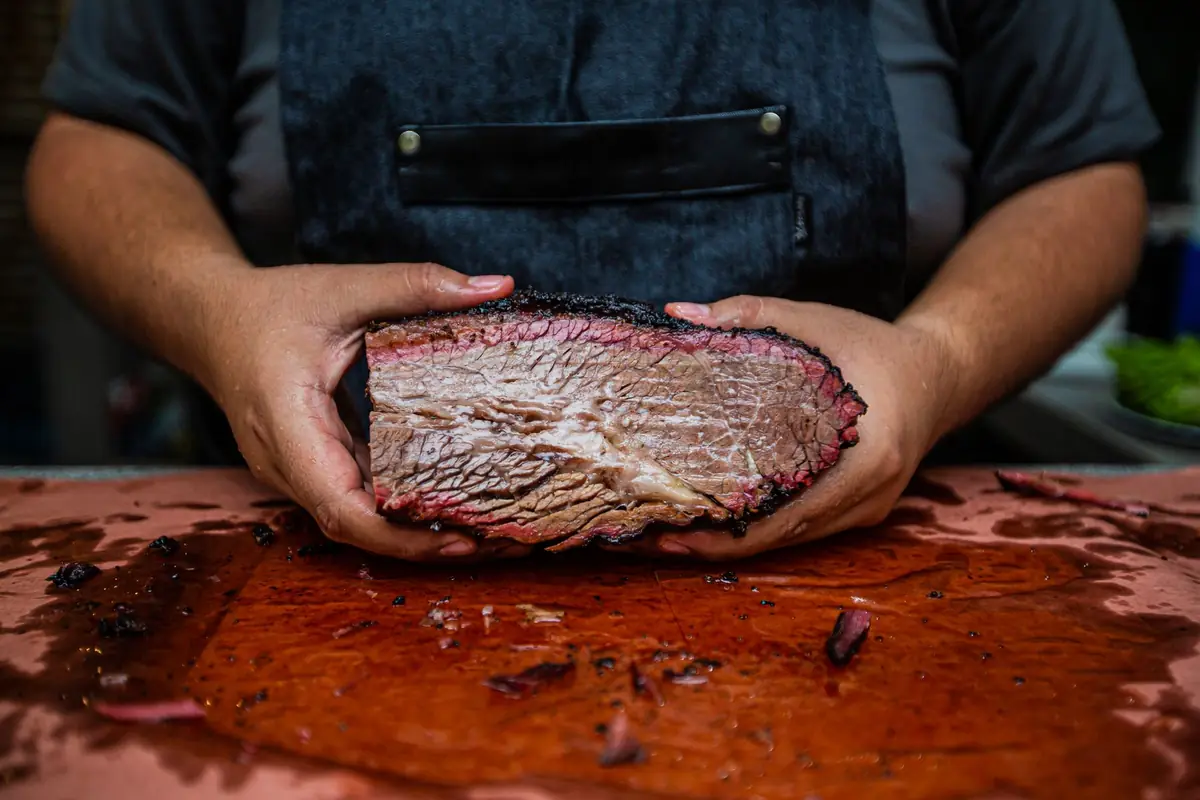 Hands holding a smoked beef brisket with a dark bark