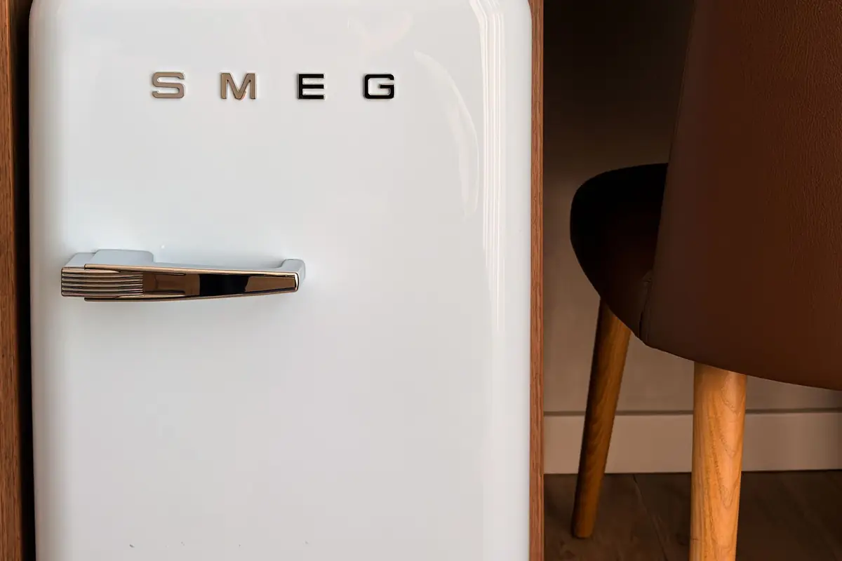 A white retro-style compact fridge next to a wooden chair