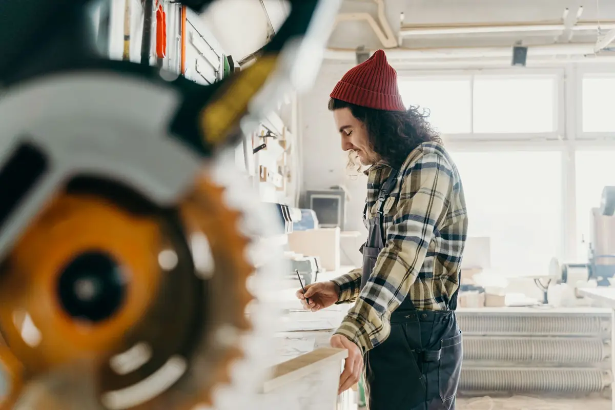 A carpenter measuring a board beside a miter saw in a workshop