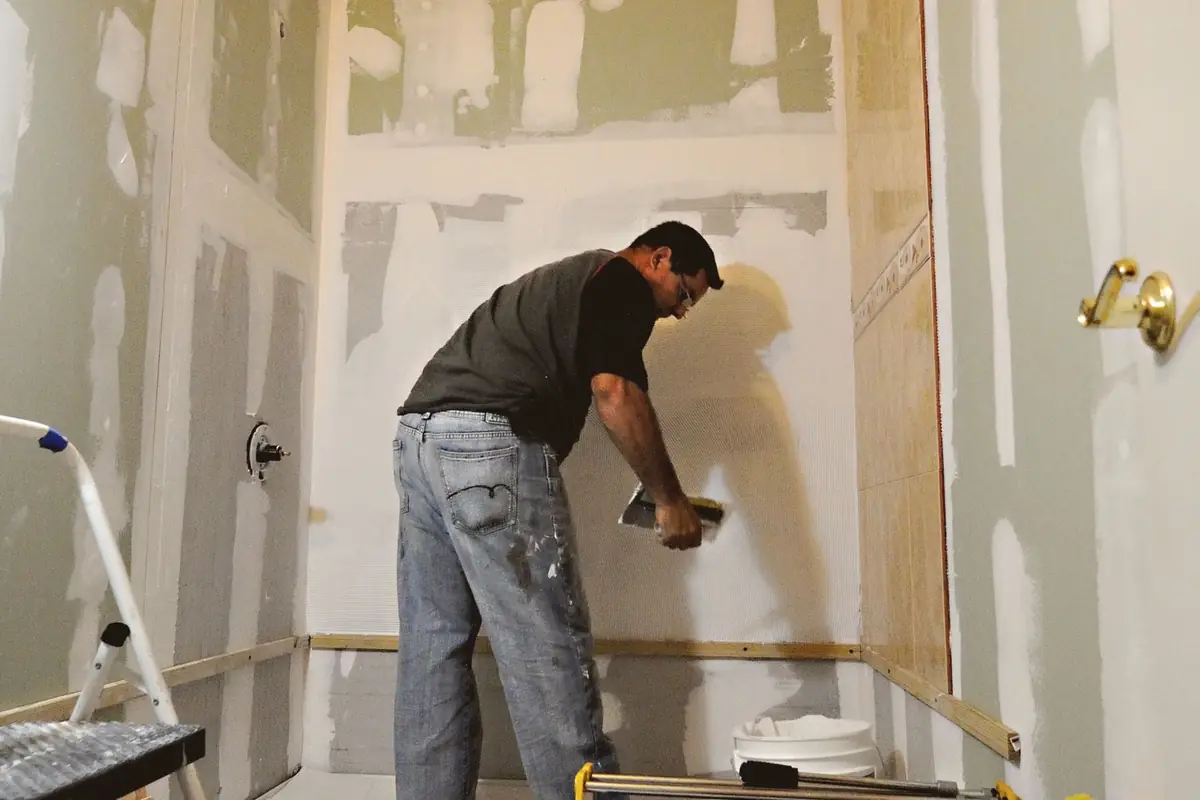 A man smoothing joint compound on a bathroom wall