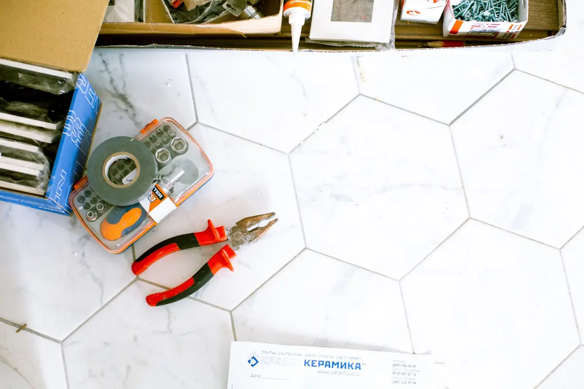 A tile cutter, pliers and spacers lying on a hexagon tile floor