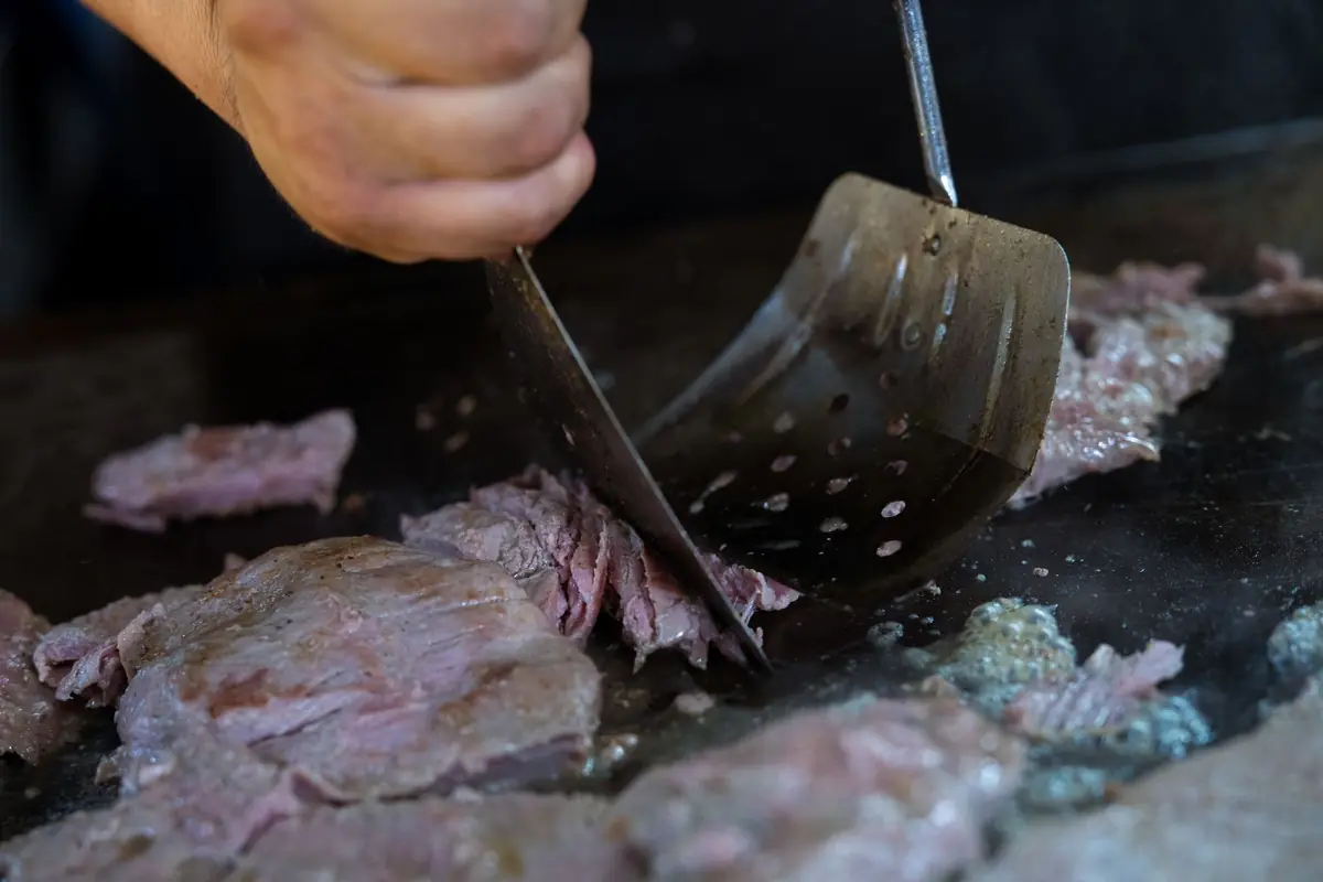 Thin slices of beef being chopped with a spatula on a hot griddle