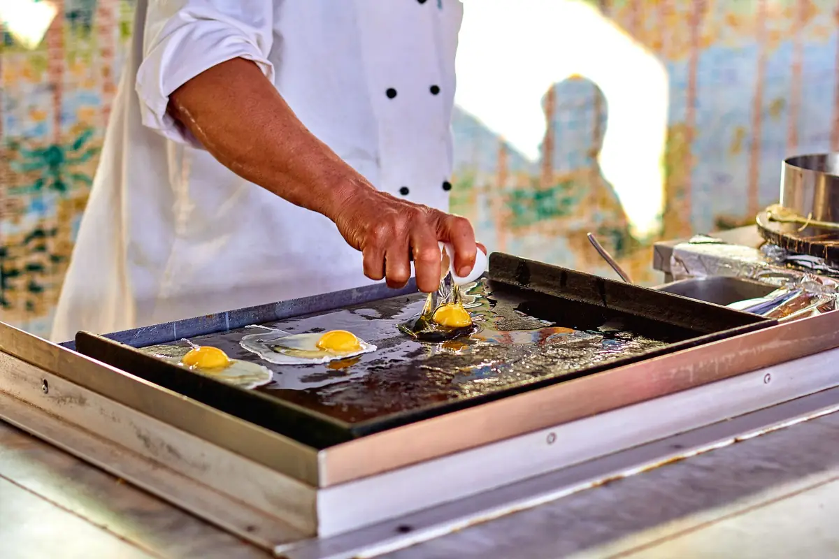 A cook frying eggs on an outdoor griddle