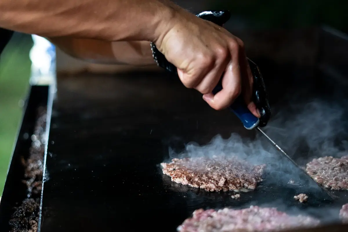 Burger patties cooking on a flat top outdoor griddle at night