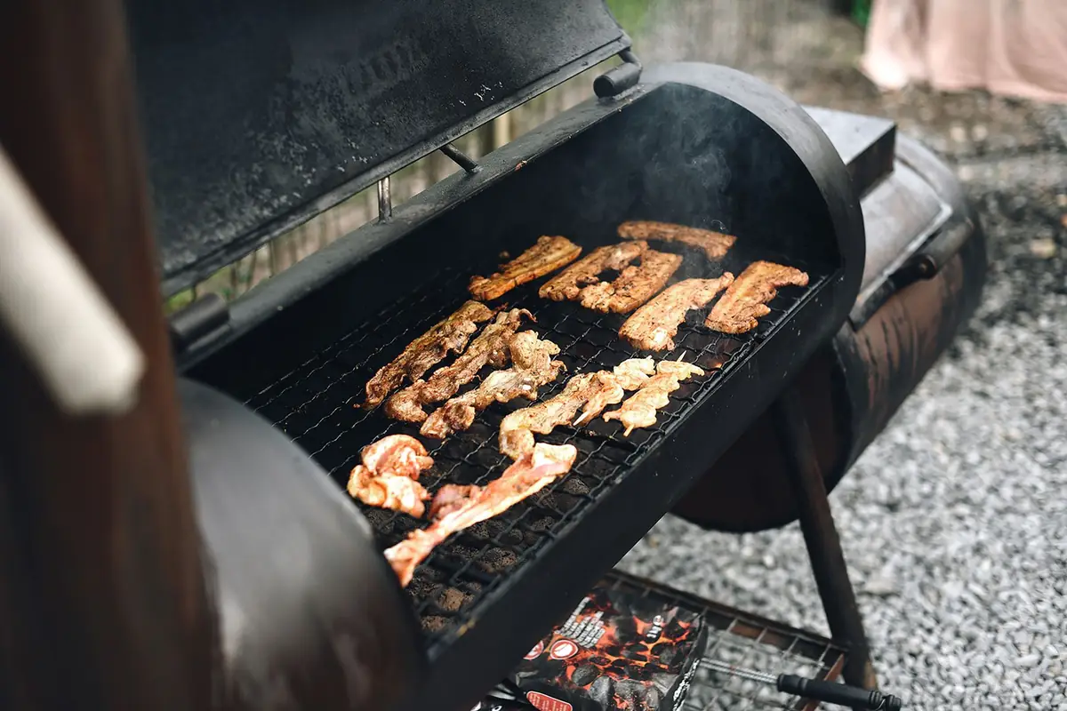 Strips of meat smoking on the grate of a barrel smoker